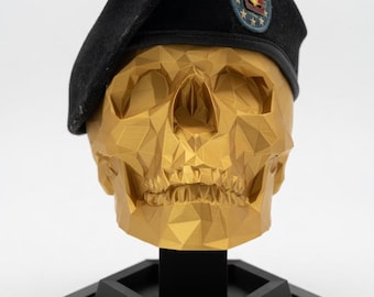 May include: A gold-colored, low-poly geometric skull sculpture wearing a black military beret with a blue and red insignia patch. The skull rests on a black hexagonal stand featuring a rectangular nameplate with the white text REAPER 7.