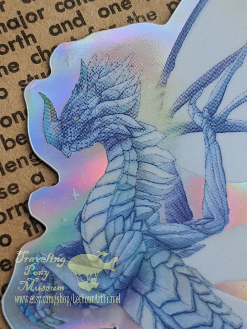 May include: A holographic sticker featuring a blue dragon with iridescent wings. The dragon is facing the left side of the image. The sticker has a white background with a faint rainbow sheen. The sticker has the text "Traveling Pony Museum" and "www.etsy.com/shop/LetYourArtTravel" at the bottom.