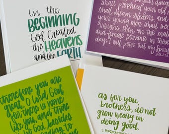 May include: A collection of square greeting cards with handwritten script. The cards feature inspirational quotes in green and white ink on various colored backgrounds, including white, green, and purple.
