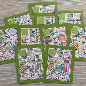 May include: A collection of handmade greeting cards with a green border. Each card features a patchwork design with cat-themed patterns, hearts, and the word "Happy". The cards are arranged on a light wood surface.