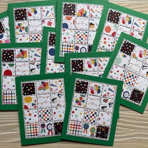 May include: A collection of handmade greeting cards with green borders. Each card features a patchwork design with colorful squares filled with festive patterns like balloons, rainbows, and confetti. The cards are arranged on a light wood surface.