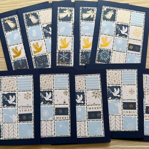 May include: A collection of handmade Christmas cards with a navy blue border. Each card features a patchwork design with images of angels, doves, snowflakes, and the words "MERRY CHRISTMAS". The color palette includes blue, white, gold, and navy.