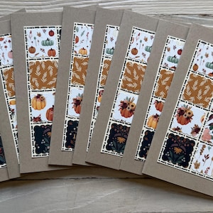 May include: A collection of handmade greeting cards with a fall theme. Each card features a patchwork design with various autumn patterns, including pumpkins, leaves, and floral motifs. The cards are set against a neutral background.