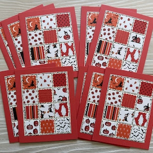 May include: A collection of red Halloween greeting cards. Each card features a patchwork design with orange, black, and white patterns, including pumpkins, bats, and witch silhouettes. The cards have a red border and are arranged on a light wood surface.