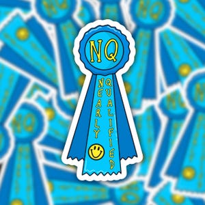May include: A blue ribbon with the text "NQ" in a yellow circle at the top and "NEARLY QUALIFIED" written vertically down the ribbon. A yellow smiley face is at the bottom of the ribbon.
