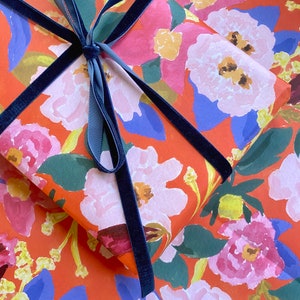 May include: A wrapped gift with floral patterned paper in shades of red, pink, blue, and green. The gift is tied with a navy blue velvet ribbon, creating a decorative bow.