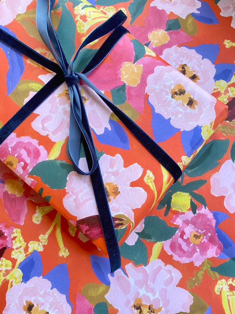 May include: A wrapped gift with floral patterned paper in shades of red, pink, blue, and green. The gift is tied with a navy blue velvet ribbon, creating a decorative bow.