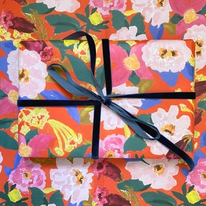 May include: A wrapped gift with floral patterned paper in shades of pink, white, yellow, and blue on a red background. The gift is tied with a dark blue velvet ribbon, creating a contrasting accent.