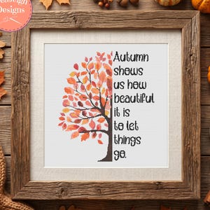 May include: Framed cross-stitch art with a tree design in autumn colors. The text reads, "Autumn shows us how beautiful it is to let things go." The frame is rustic, and the background includes pumpkins and leaves.