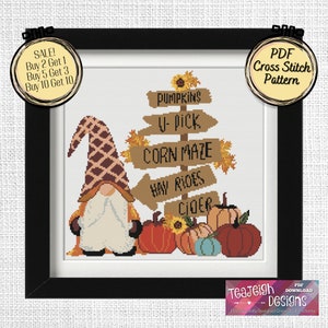Könnte beinhalten: Kreuzstichmuster mit einem Zwerg, der vor einem Holzschild mit den Worten "Pumpkins, U-pick, Corn Maze, Hay Rides, Cider" steht. Der Zwerg trägt einen braunen Hut und einen weißen Bart. Um den Zwerg herum befinden sich Kürbisse und Sonnenblumen.