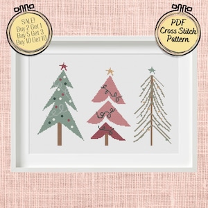 Puede incluir: Un patrón de punto de cruz con tres árboles de Navidad estilizados. Los árboles están decorados con adornos y luces rojas, rosas y verdes. El patrón está disponible para descargar en PDF.