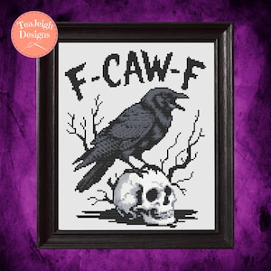 May include: Framed cross-stitch art featuring a black crow perched atop a skull, with the text "F-CAW-F" above. The artwork is set against a white background and framed in a dark wooden frame. The design has a gothic theme.