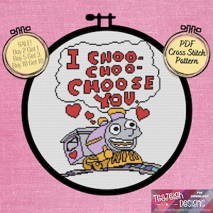 Op de afbeelding: Een kruissteekpatroon met een cartoon-trein met een hartvormig gezicht en de tekst "I choo-choo-choose you." Het patroon is in een ronde hoepel met een roze achtergrond.
