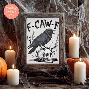 May include: Cross-stitch artwork in a wooden frame featuring a black crow perched on a skull, with the text "F-CAW-F". The artwork is surrounded by candles, pumpkins, and spiderwebs, creating a Halloween theme.