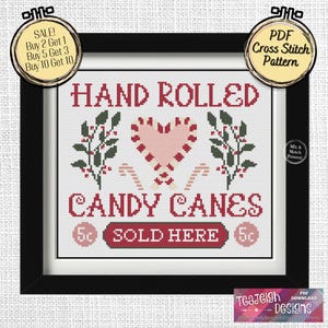 May include: A cross stitch pattern for a sign that reads "Hand Rolled Candy Canes 5c Sold Here 5c". The sign features a heart-shaped candy cane, holly sprigs, and candy canes.