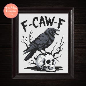 May include: Framed cross-stitch art featuring a black crow perched atop a skull, with the text "F-CAW-F" above. The artwork is set against a white background and framed in a dark brown wooden frame. The design includes bare branches.