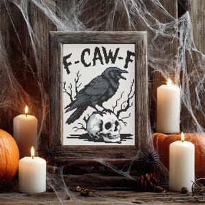May include: A framed cross-stitch depicting a black crow atop a skull, with the text "F-CAW-F". The image is set against a rustic wooden backdrop, with lit candles, pumpkins, and cobwebs, creating a Halloween theme.
