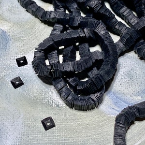 May include: Abstract composition featuring dark, textured, interconnected shapes and three small square elements with central white dots. The shapes appear to be made of stacked, rectangular pieces, creating a layered effect. The background is a blend of gray and white.