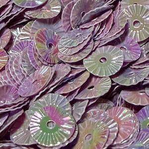 May include: A collection of small, circular, lavender-colored sequins with a scalloped edge and a central hole. Each sequin features a reflective, iridescent finish that creates a shimmering effect with hints of green and pink light.