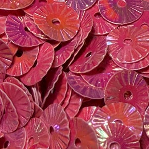 May include: A collection of circular, hot pink sequins with a pleated, fan-like texture and a central hole. Each sequin features an iridescent, reflective finish that catches the light, creating a vibrant, layered display of bright pink tones.