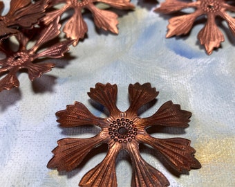 Può includere: Primo piano di diversi abbellimenti metallici a forma di fiore color rame. Ogni fiore ha dettagliati disegni di petali e centro. Gli abbellimenti sono sparsi su una superficie dipinta di azzurro chiaro e bianco.