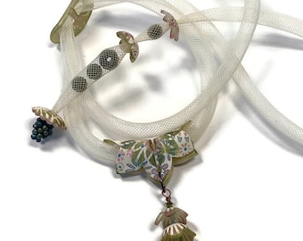 May include: A unique necklace featuring a white mesh cord with decorative elements. The necklace includes floral and geometric accents in shades of green, pink, and brown. A pendant with layered floral shapes hangs from the center, adding a whimsical touch.