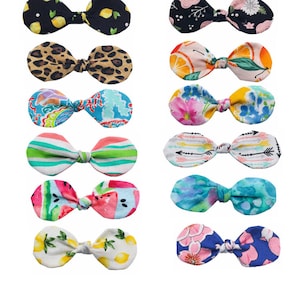 May include: Twelve different fabric hair bows with various patterns, including lemons, leopard print, floral, stripes, watermelon, and arrows. The bows are all tied in a knot and are a light pink, blue, green, yellow, and white.