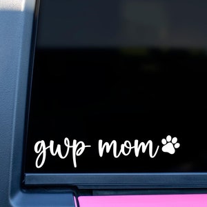 May include: A white vinyl decal with the text "gwp mom" and a paw print on a black background. The decal is on the back window of a pink car.