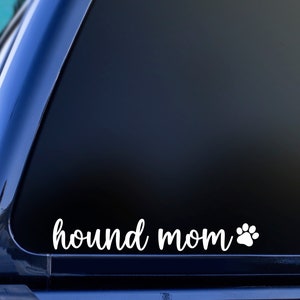 May include: A white vinyl decal with the text "hound mom" and a paw print on a black car window.