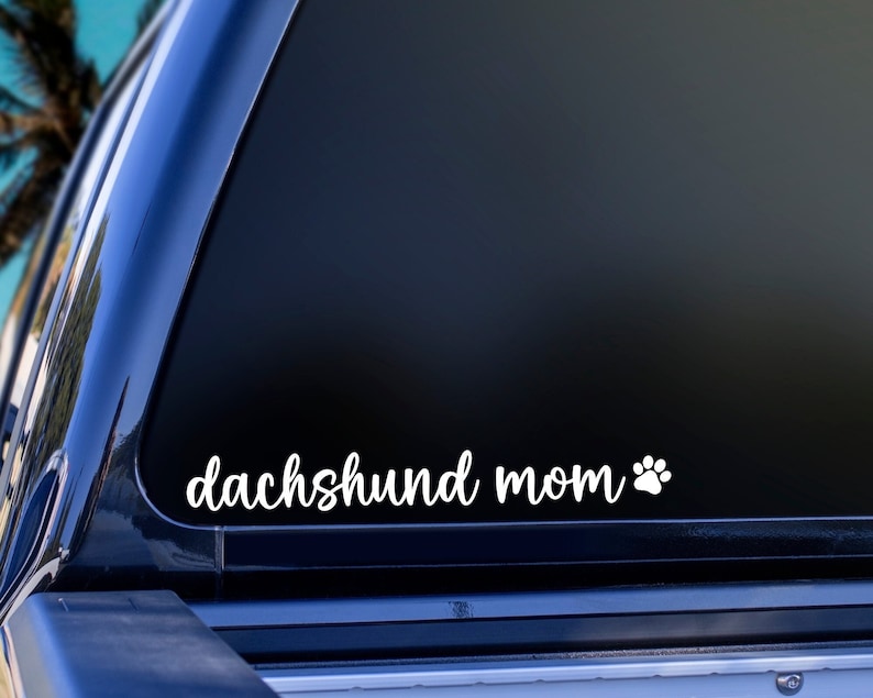 White Dachshund Mom decal with a paw print placed on the window of a car.