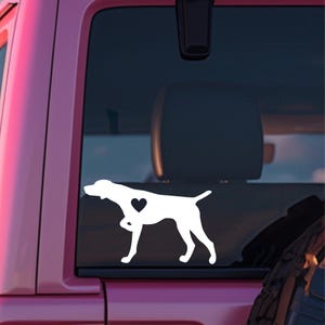 May include: White vinyl decal of a German Shorthaired Pointer dog silhouette with a heart on its chest, displayed on the back window of a pink car.