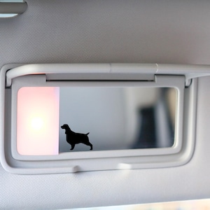 May include: A white car visor with a built-in mirror and a light. A black silhouette of a dog is visible in the mirror.