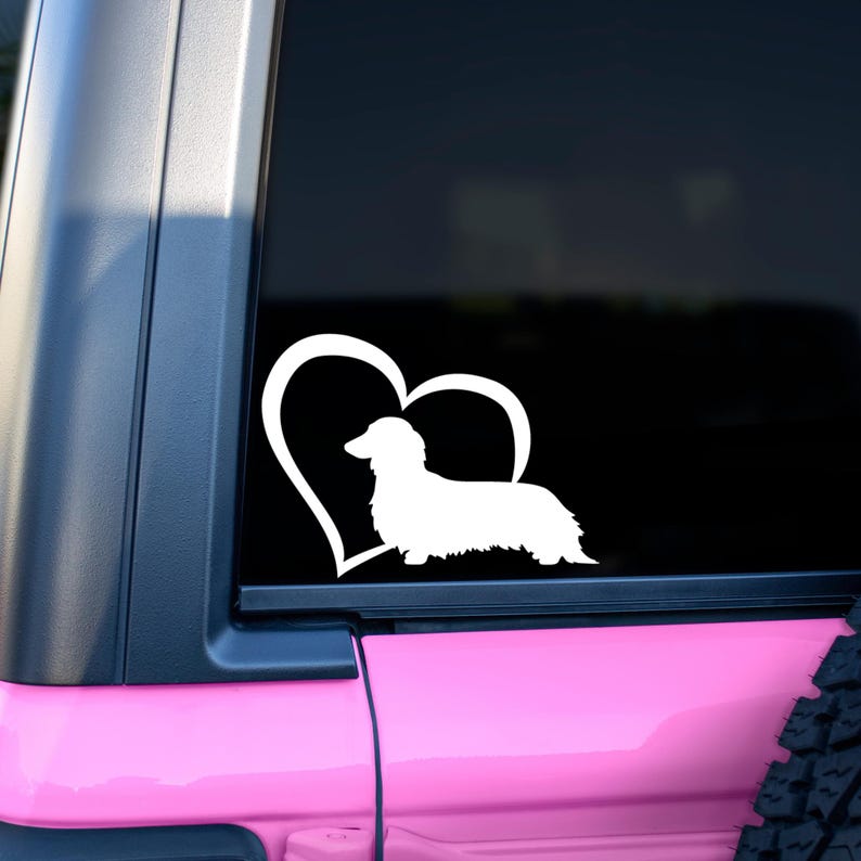 White Long Haired Dachshund decal with a heart placed on the window of a car.