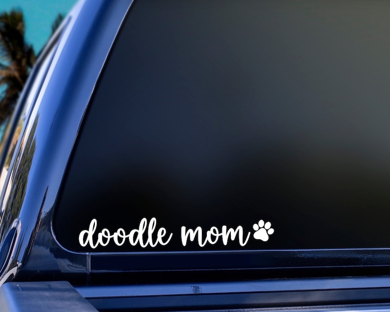 White Doodle Mom decal with a paw print placed on the window of a car.