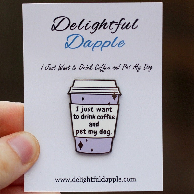 A purple and white coffee cup enamel pin with the phrase “I just want to drink coffee and pet my dog.”