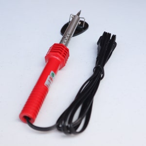 May include: A red soldering iron with a black cord and a stand. The soldering iron has a metal tip and a black plastic handle.