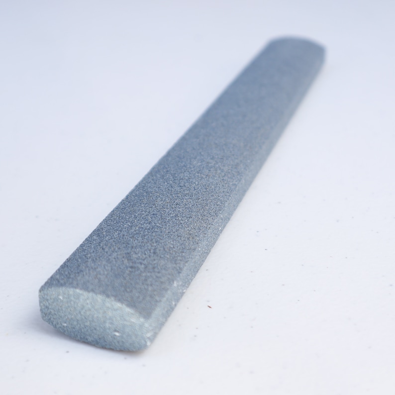 May include: A gray, rectangular sharpening steel with a rounded end. The steel is made of a rough, textured material.