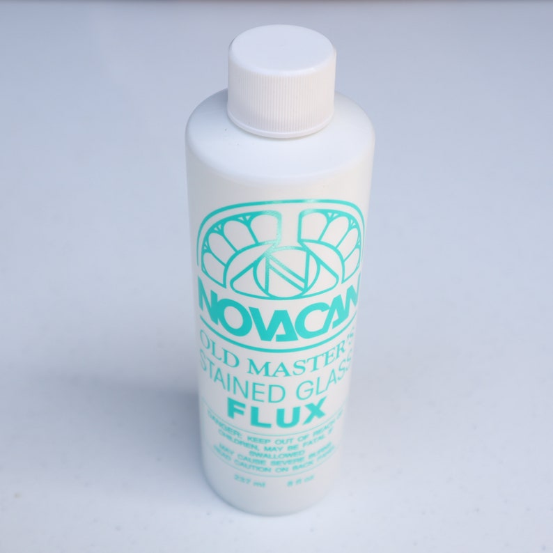 May include: A white bottle of Novacan Old Master Stained Glass Flux. The bottle has a turquoise label with the company logo and the product name.
