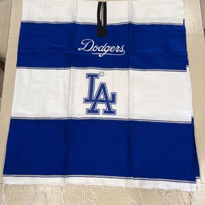 May include: A white and blue striped throw blanket with the words "Dodgers" and "LA" embroidered on it. The blanket has a fringe border.