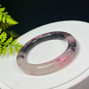 May include: A white, pink, and black jade bangle bracelet. The bracelet is made of polished jade and has a smooth, rounded surface.