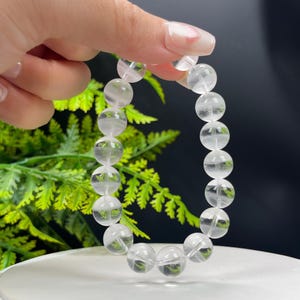 Może przedstawiać: Bransoletka z przezroczystych koralików z kryształu górskiego o okrągłym kształcie. Bransoletka wykonana jest z naturalnych kamieni i jest popularnym wyborem biżuterii.