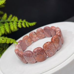 Könnte beinhalten: Ein rosafarbenes und weißes fossiles Korallenarmband mit polierter Oberfläche. Das Armband besteht aus ovalen Perlen mit einem einzigartigen Muster.