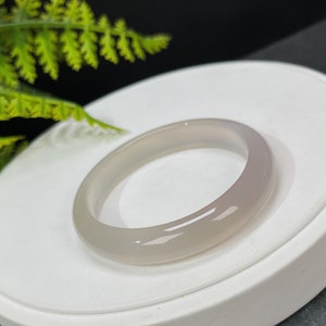 May include: A smooth, white jade bangle bracelet. The bangle is made of a light, translucent material and has a polished finish.