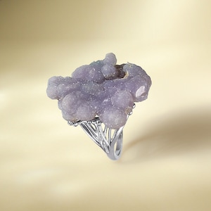 May include: A silver ring featuring a large, purple agate gemstone. The gemstone is irregularly shaped and has a rough, textured surface.