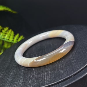 May include: A white, brown, and yellow agate bangle bracelet. The bracelet is smooth and polished.