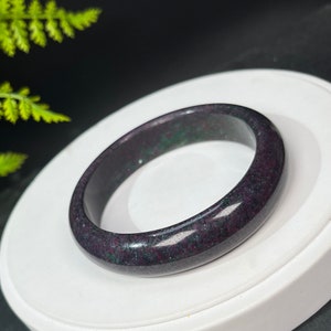 May include: A dark purple and green jade bangle bracelet. The bangle is smooth and polished, with a speckled pattern.