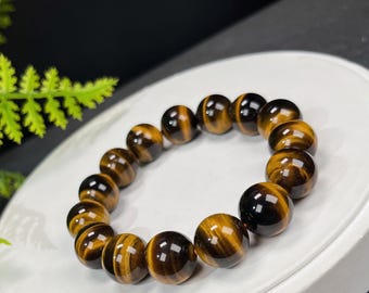 May include: A bracelet featuring polished, round tiger's eye beads. The beads are a mix of golden brown and dark brown, with a glossy finish. The bracelet is displayed on a white surface.