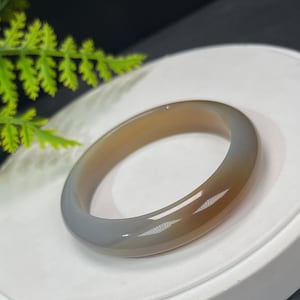 May include: A gray and brown agate bangle bracelet. The bracelet is smooth and polished, with a subtle swirl pattern.
