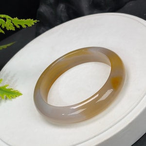 May include: A polished, oval-shaped bracelet in shades of amber and grey. The gemstone bracelet has a smooth, glossy finish. The bracelet is a piece of jewellery.