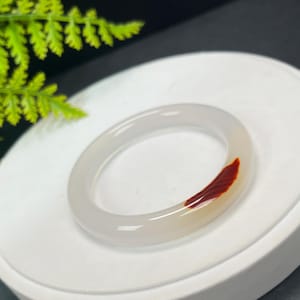 May include: White jade bangle with a red and white agate inlay. The bangle is smooth and polished.